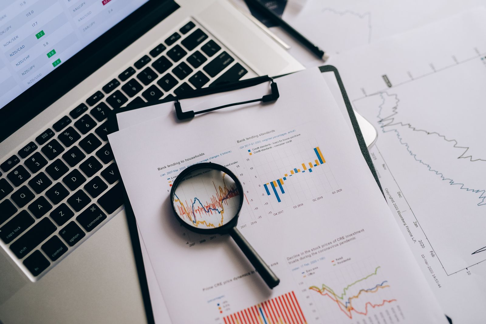 Magnifying glass over printed charts beside a laptop keyboard, a visual for how to choose keywords for a business website